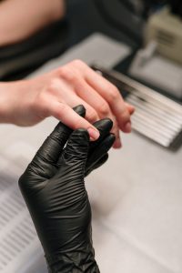 About A professional manicurist wearing black gloves provides a manicure service to a client.